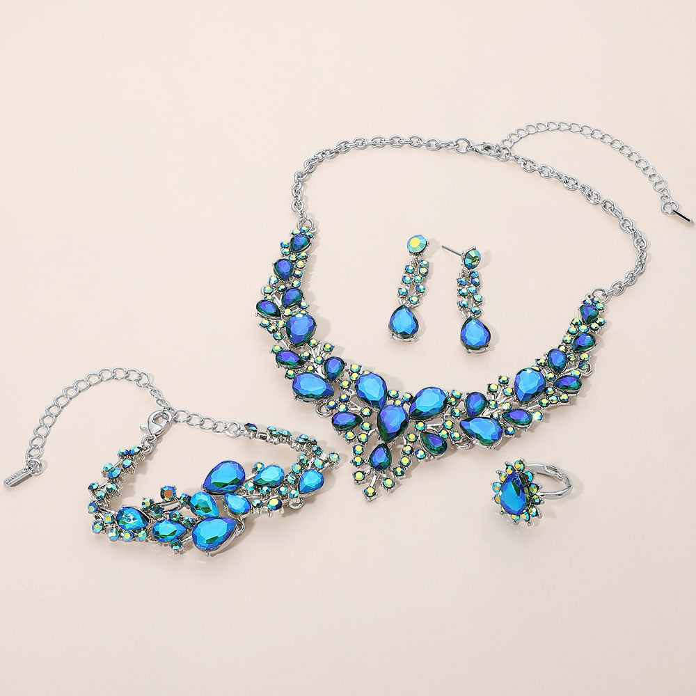Blue AB crystal 4-piece jewelry set on silver with statement necklace, matching bracelet, drop earrings and adjustable ring arranged on a light beige background.