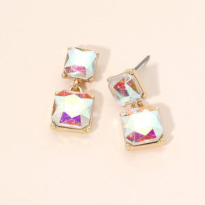 AB iridescent crystal double-square drop earrings on gold-tone metal, each featuring a smaller faceted square stone connected to a larger square stone below, reflecting rainbow colors. Each earring measures approximately 0.4 inches wide by 0.9 inches long. Displayed on a pale peach surface.