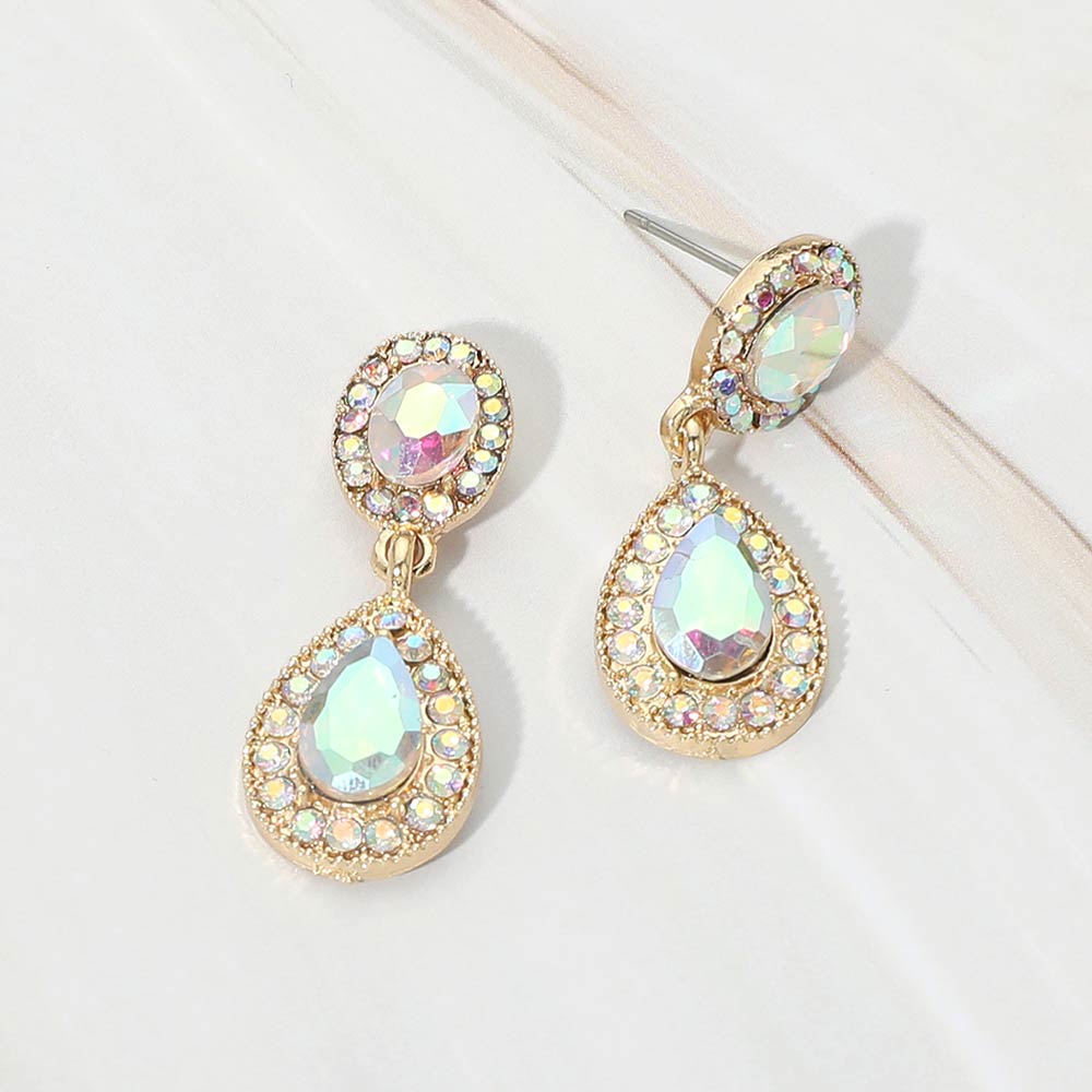 A pair of gold-tone teardrop dangle earrings with AB crystal center stones surrounded by smaller clear rhinestones, displayed on a white marble surface.