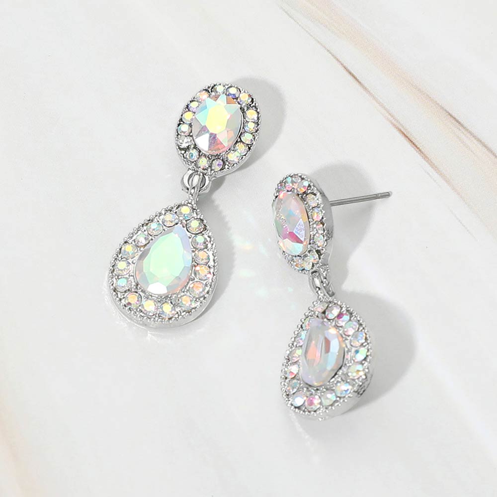 A pair of silver-tone teardrop dangle earrings with AB crystal center stones surrounded by smaller clear rhinestones, displayed on a white marble surface.