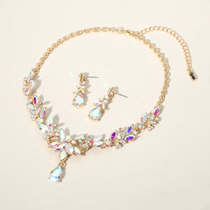 AB crystal teardrop and marquise leaf necklace set on gold with matching earrings, iridescent statement jewelry for prom and evening wear on a beige background