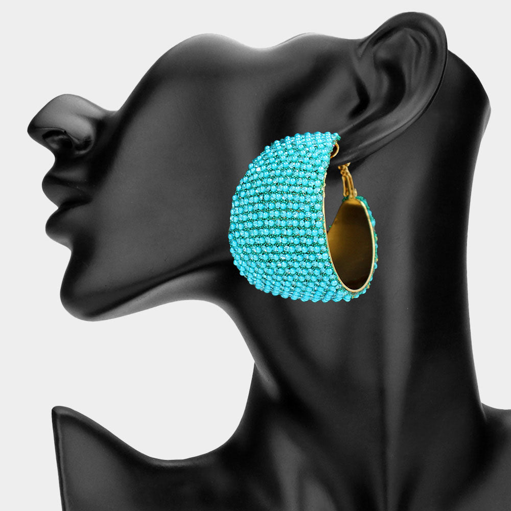 Aqua bling pavé crystal wide hoop earrings on gold-tone metal with dense faceted rhinestone coverage and omega backs, displayed on a black mannequin profile.