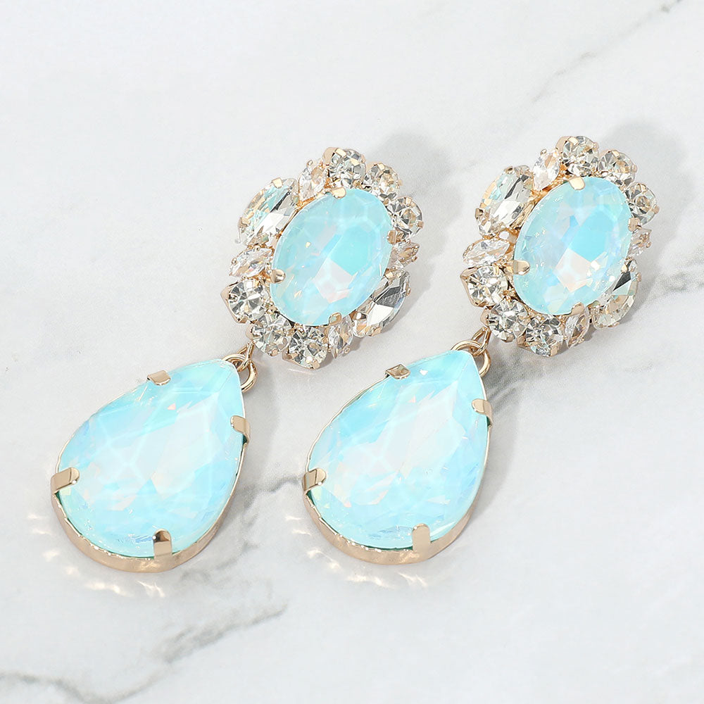Aqua oval and teardrop earrings with clear crystal accents on gold on a white marble background
