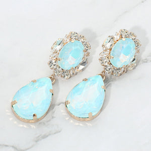 Aqua oval and teardrop earrings with clear crystal accents on gold on a white marble background