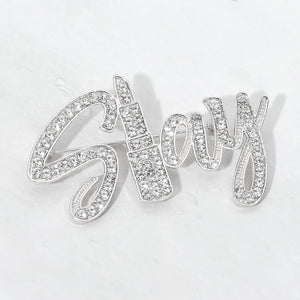 Silver-tone “Slay” brooch with clear crystals covering flowing, connected script lettering, measuring approximately 2.6 inches wide by 1.5 inches tall, displayed on a white background.