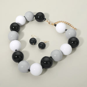 Black, white, and grey chunky ball beaded statement necklace set with oversized round beads and matching earrings, displayed on a beige background.