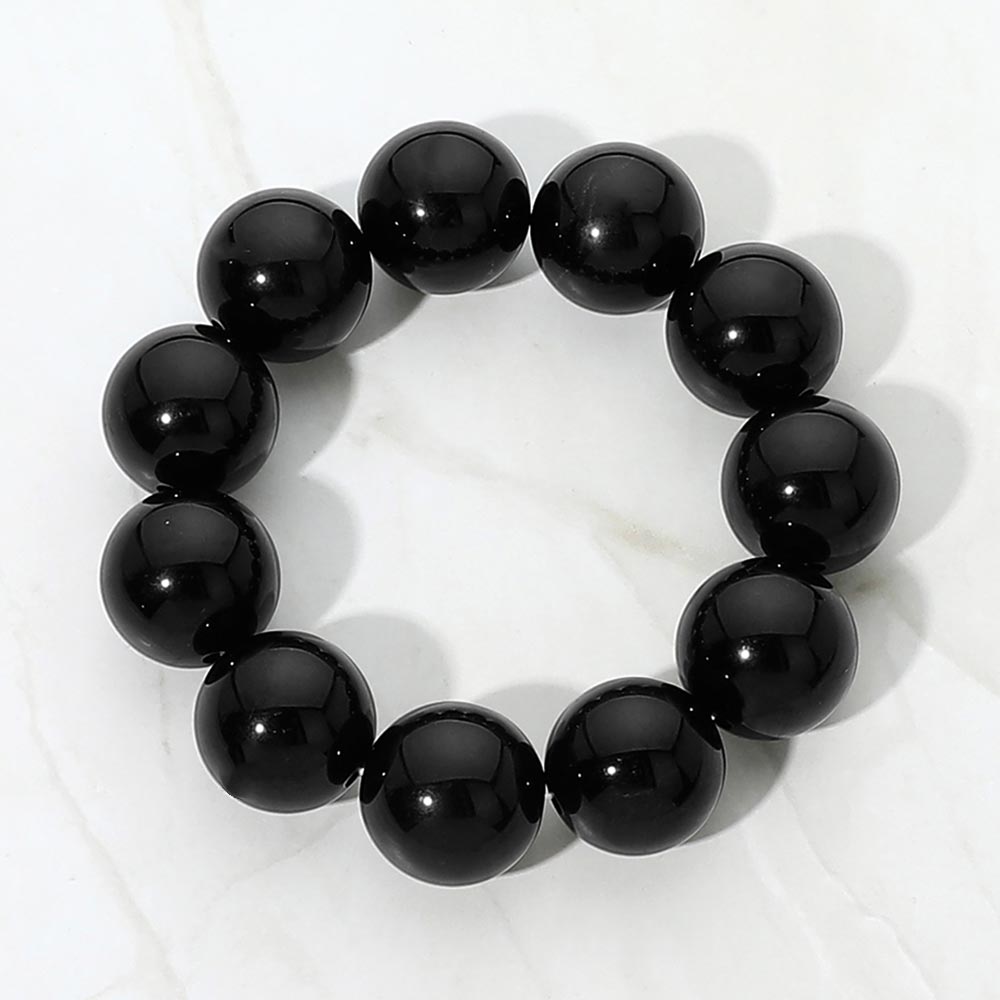 Black chunky ball beaded stretch bracelet with oversized round beads, displayed on a white marble background.