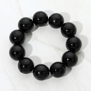 Black chunky ball beaded stretch bracelet with oversized round beads, displayed on a white marble background.