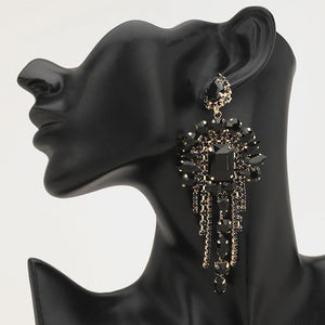 Long 4.6" black chandelier fringe earrings on gold on a black mannequin ear — dramatic crystal statement jewelry for pageant, prom, weddings, and evening events.