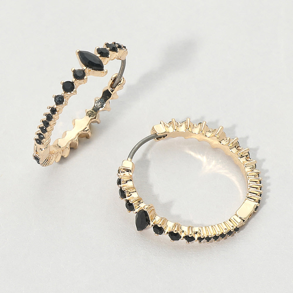A pair of gold huggie hoop earrings with black marquise and round gemstones, displayed on a light gray background.