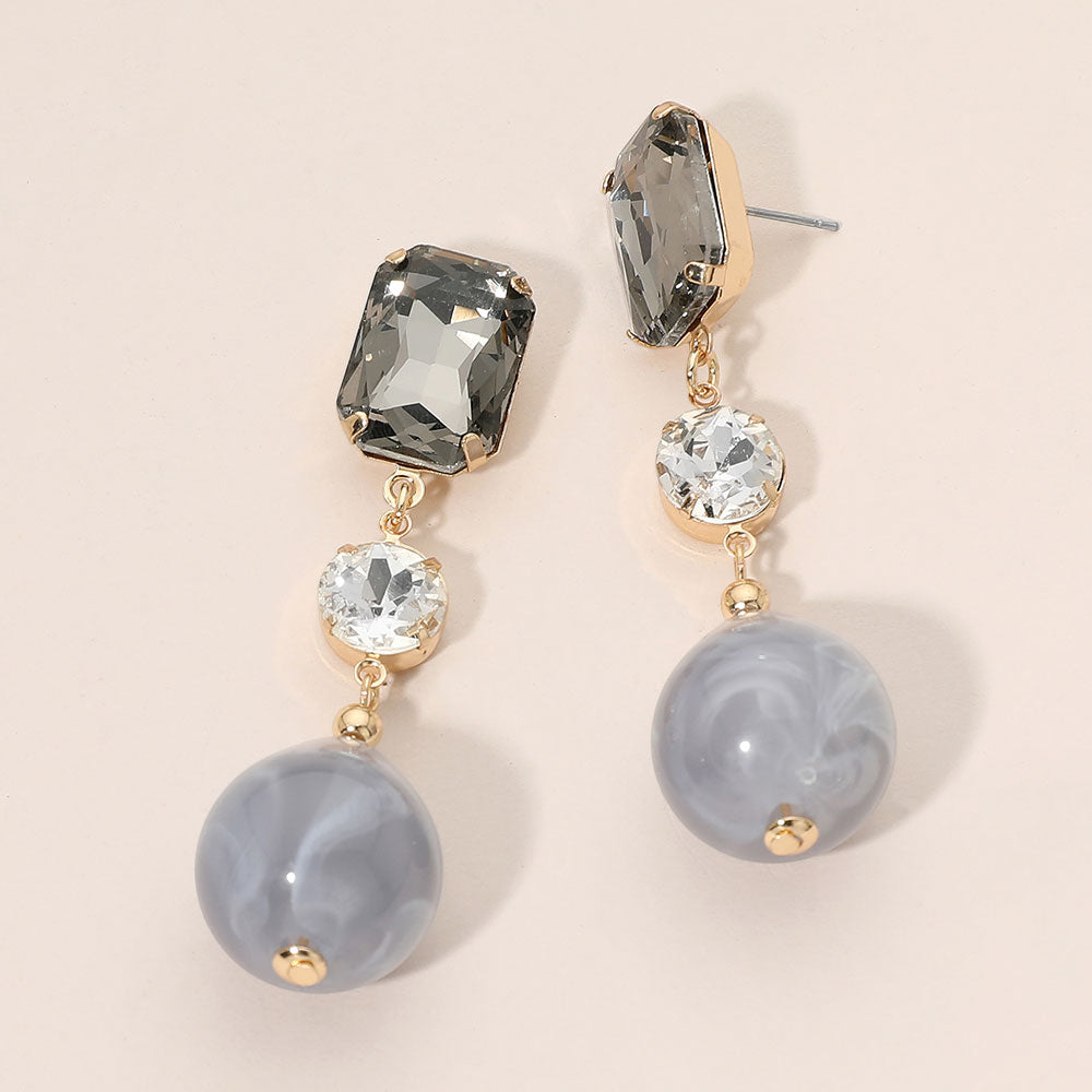 Gray faceted crystal and ball drop statement earrings on gold with rectangular, round, and spherical gray stones, displayed on a light beige background.