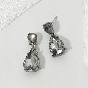 Double teardrop dangle earrings with gray crystals on gunmetal, featuring smaller faceted teardrops above larger teardrop drops, displayed on a white textured surface.