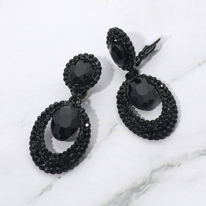Black oval double-halo crystal clip-on earrings on a white marble background — 2.1" statement drops for evening or pageant glam.