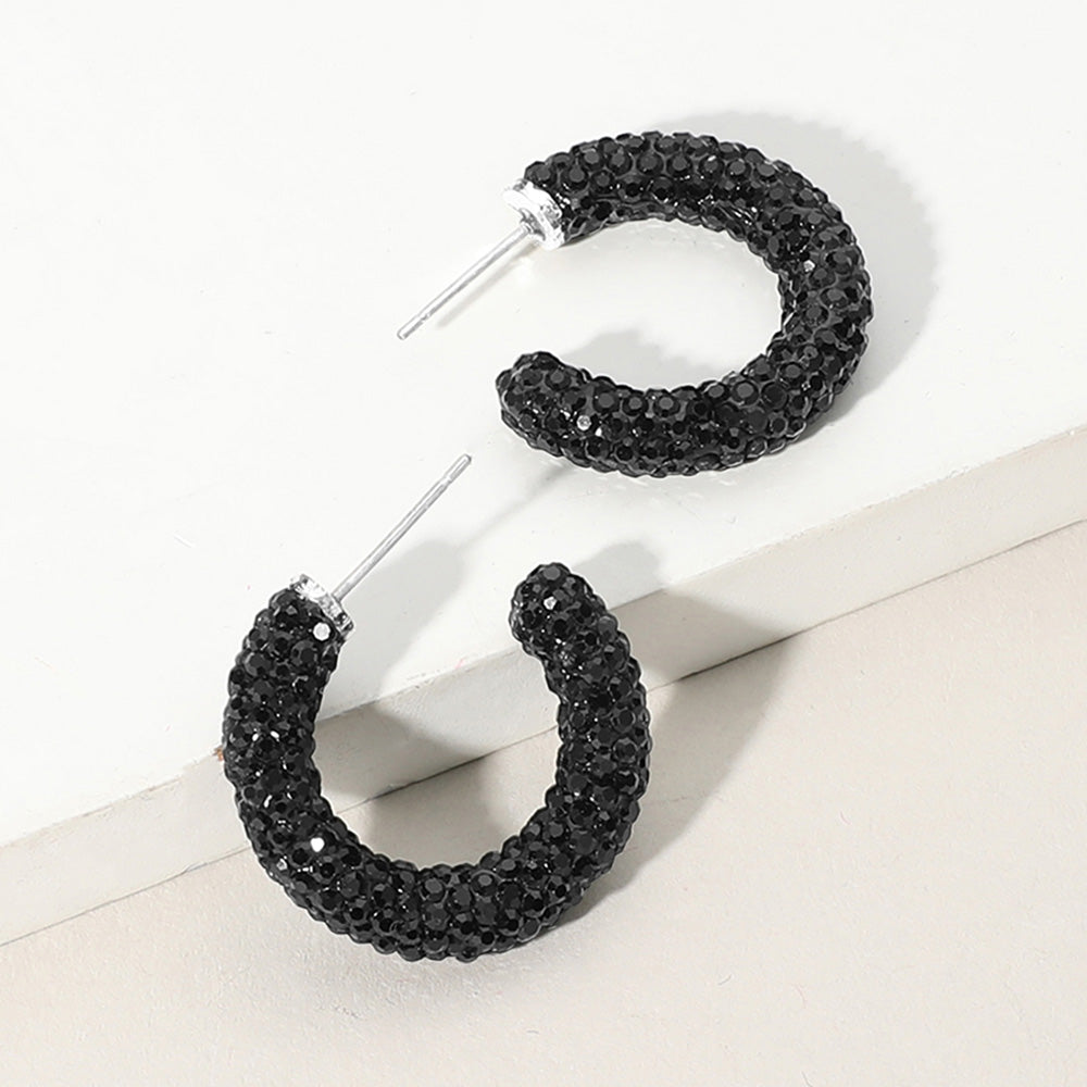 Black pavé half hoop earrings in a silver finish featuring rows of black rhinestones covering the front of each hoop, displayed on a light beige background.