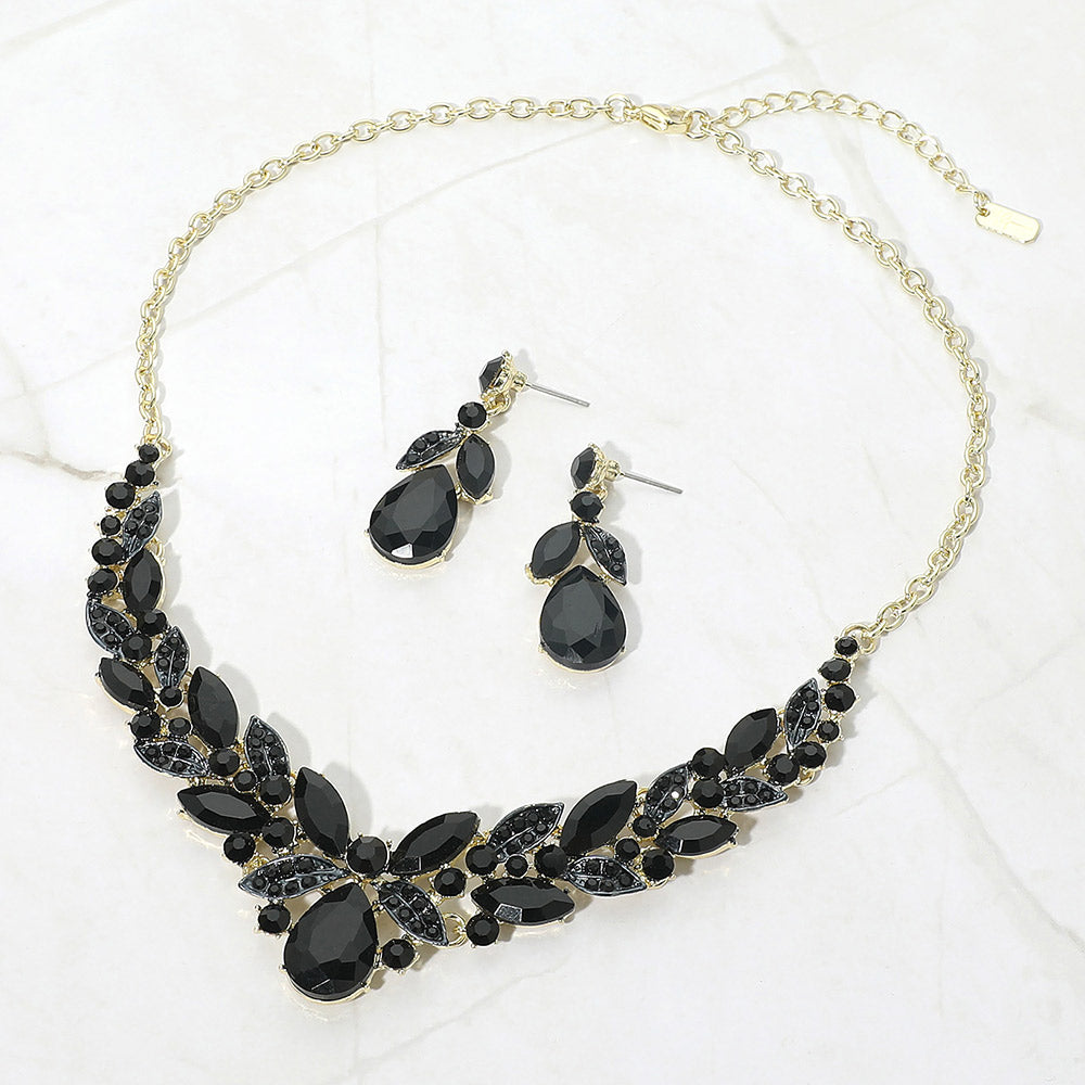 Black teardrop and marquise crystal jewelry set on gold displayed on white marble background