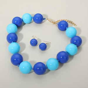 Blue and Light Blue chunky ball beaded statement necklace set with oversized round beads and matching earrings, displayed on a beige background.