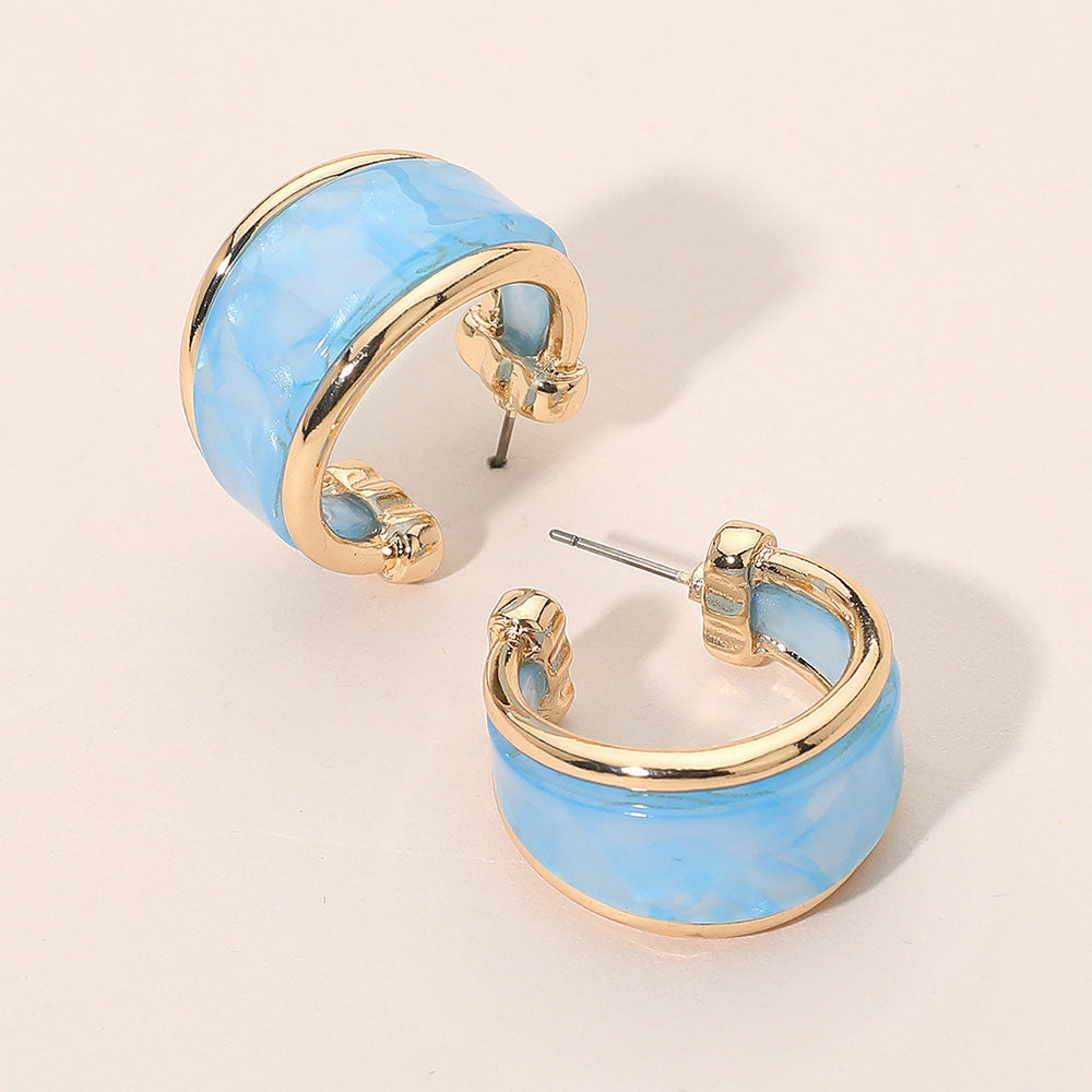 Blue marbled resin half hoop earrings with wide chunky statement design trimmed in gold for fun fashion and everyday wear on a light beige background
