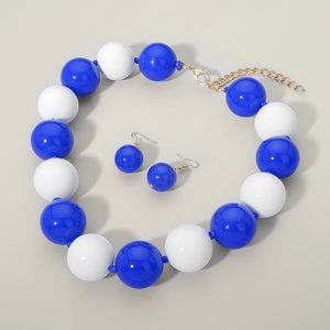 Blue and white chunky ball beaded statement necklace set with oversized round beads and matching earrings, displayed on a beige background.