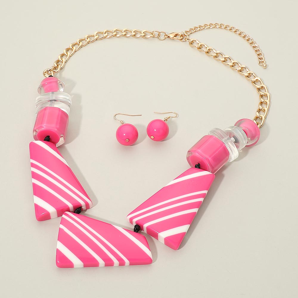 Fuchsia Hot Pink geometric statement necklace set with oversized striped shapes, round bead accents, matching earrings, and gold chain, displayed on a light cream background.