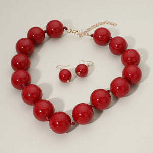 Burgundy chunky ball beaded statement necklace set with oversized round beads and matching drop earrings, displayed on a light cream background.