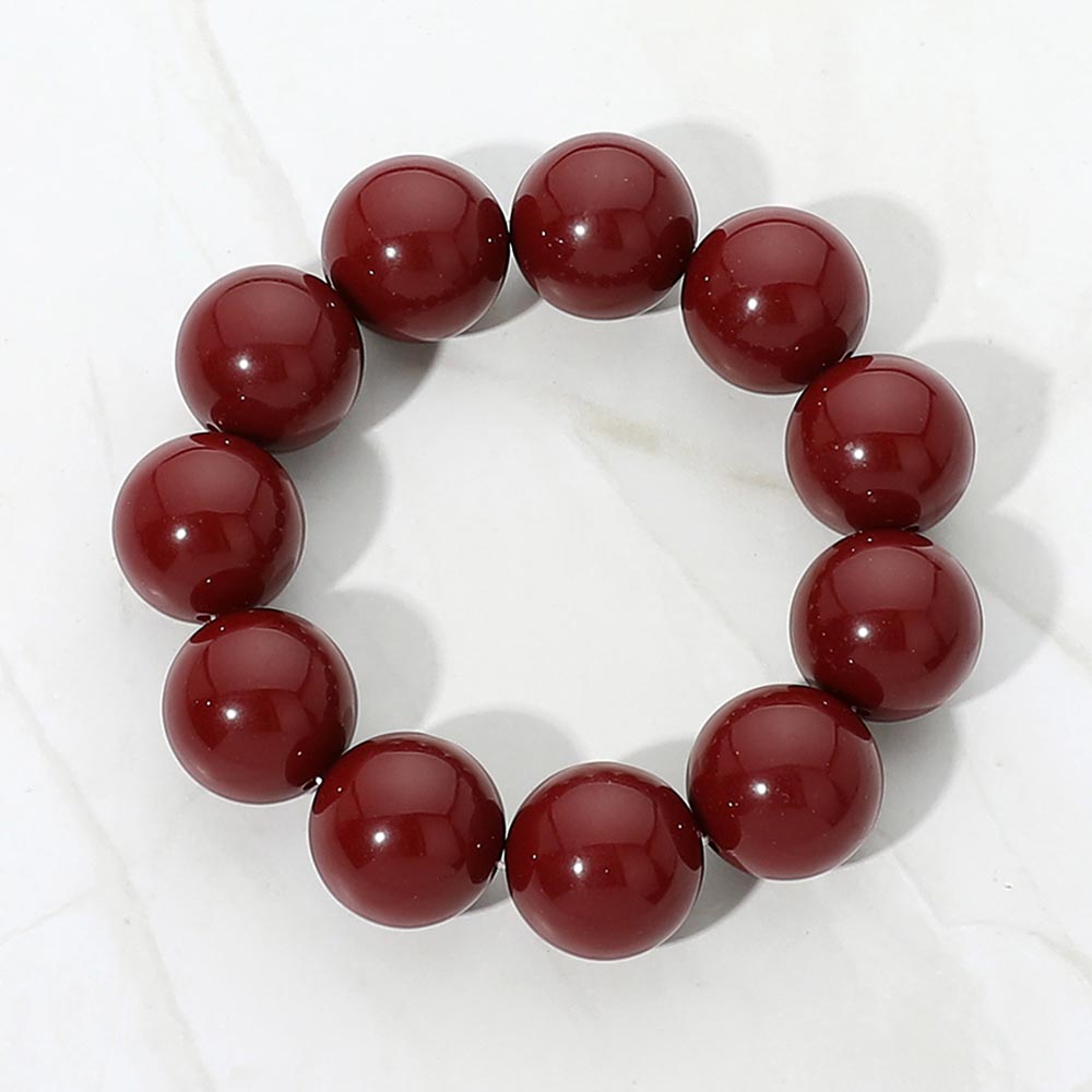 Burgundy chunky ball beaded stretch bracelet with oversized round beads, displayed on a white marble background.