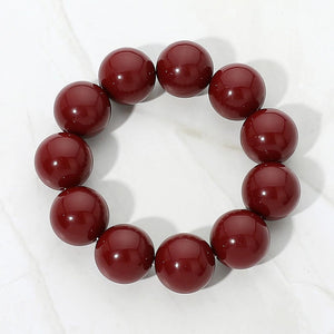 Burgundy chunky ball beaded stretch bracelet with oversized round beads, displayed on a white marble background.