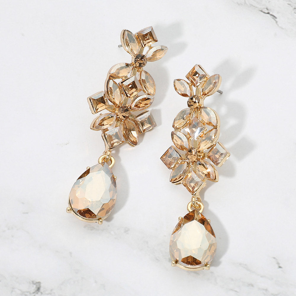 Champagne gold-colored crystal floral teardrop earrings on gold-tone metal, featuring clusters of marquise, square, and round stones above large faceted teardrop drops. Each earring measures approximately 0.8 inches wide by 2.5 inches long. Displayed on a white marble surface with gray veining.