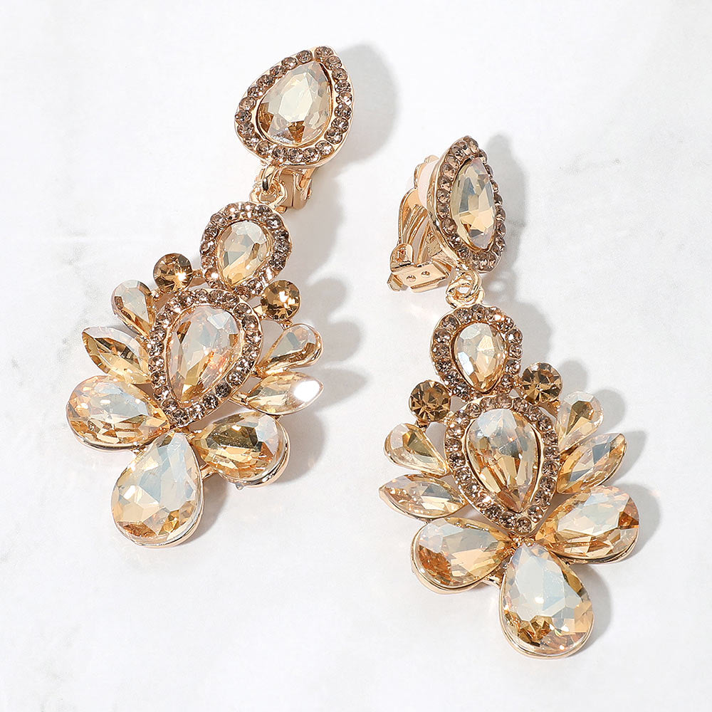 A pair of gold-tone chandelier clip-on earrings with champagne gold teardrop and oval faceted crystals surrounded by smaller rhinestones, displayed on a white marble surface.
