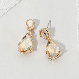 Double teardrop dangle earrings with champagne gold crystals on gold, measuring 1 inch long by 0.4 inch wide, featuring smaller faceted teardrops above larger drops, displayed on a white textured surface.