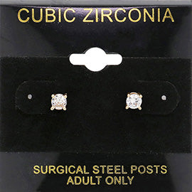 Classic round clear crystal stud earrings in a gold finish with prong settings and surgical steel posts, displayed on a black jewelry card.
