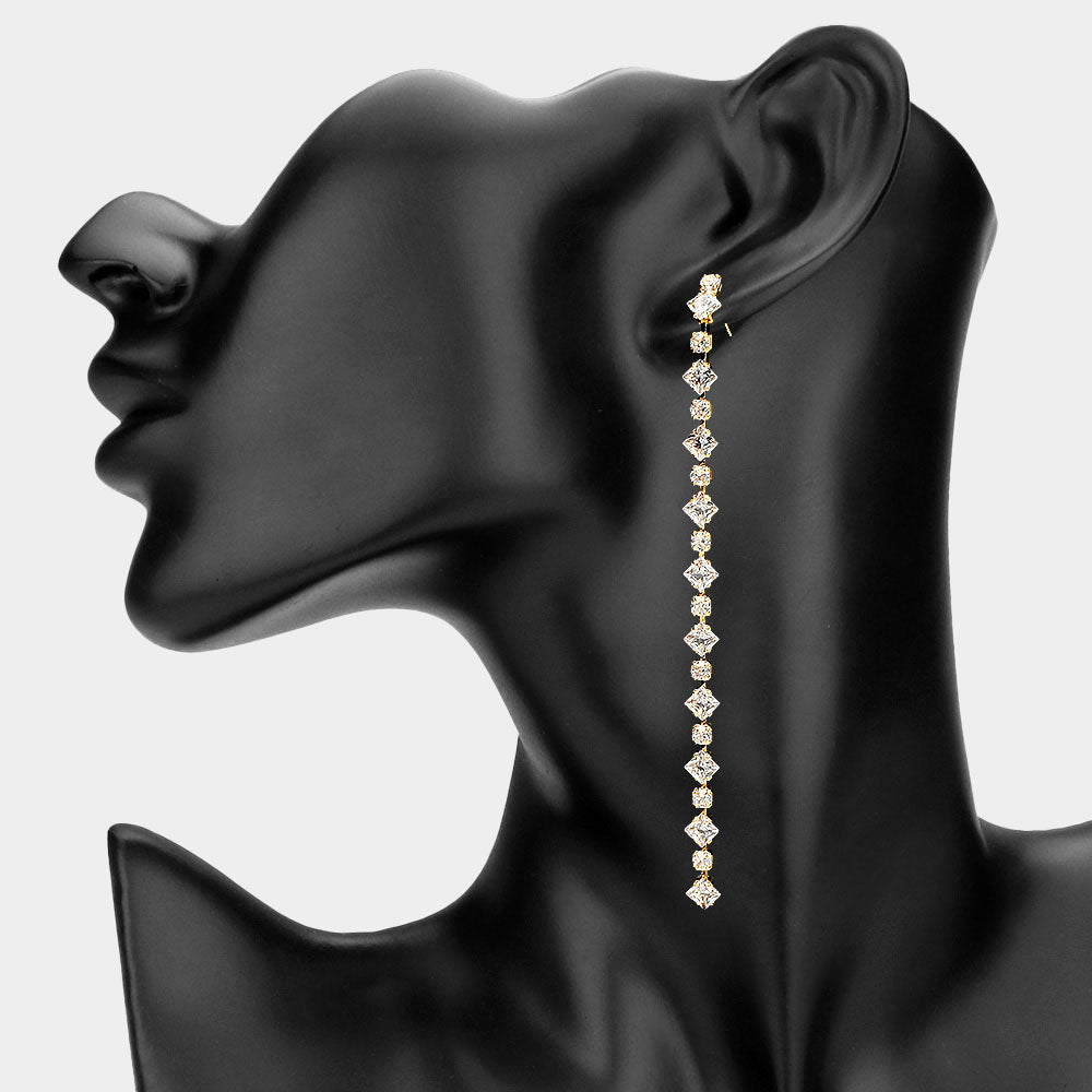 Long geometric crystal link drop earrings in a gold finish featuring a vertical row of clear crystals, displayed on a black model ear.