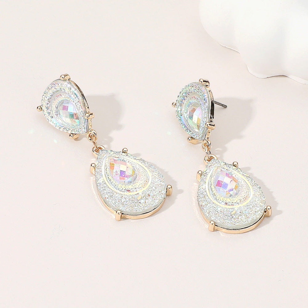 Clear and AB crystal glitter teardrop drop earrings on gold on light beige background