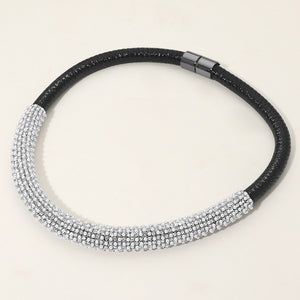 Clear crystal rhinestone studded formal necklace on black with a textured crystal-covered front section and magnetic closure, displayed on a light beige background.