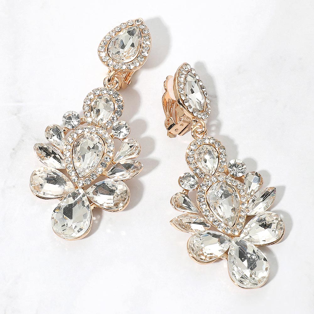 Gold-tone chandelier clip-on earrings with clear teardrop and oval faceted crystals surrounded by smaller clear rhinestones, displayed on a white marble surface.