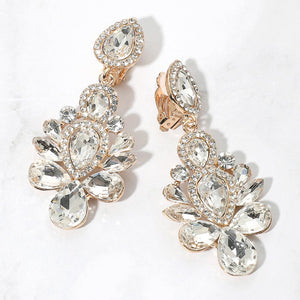 Gold-tone chandelier clip-on earrings with clear teardrop and oval faceted crystals surrounded by smaller clear rhinestones, displayed on a white marble surface.