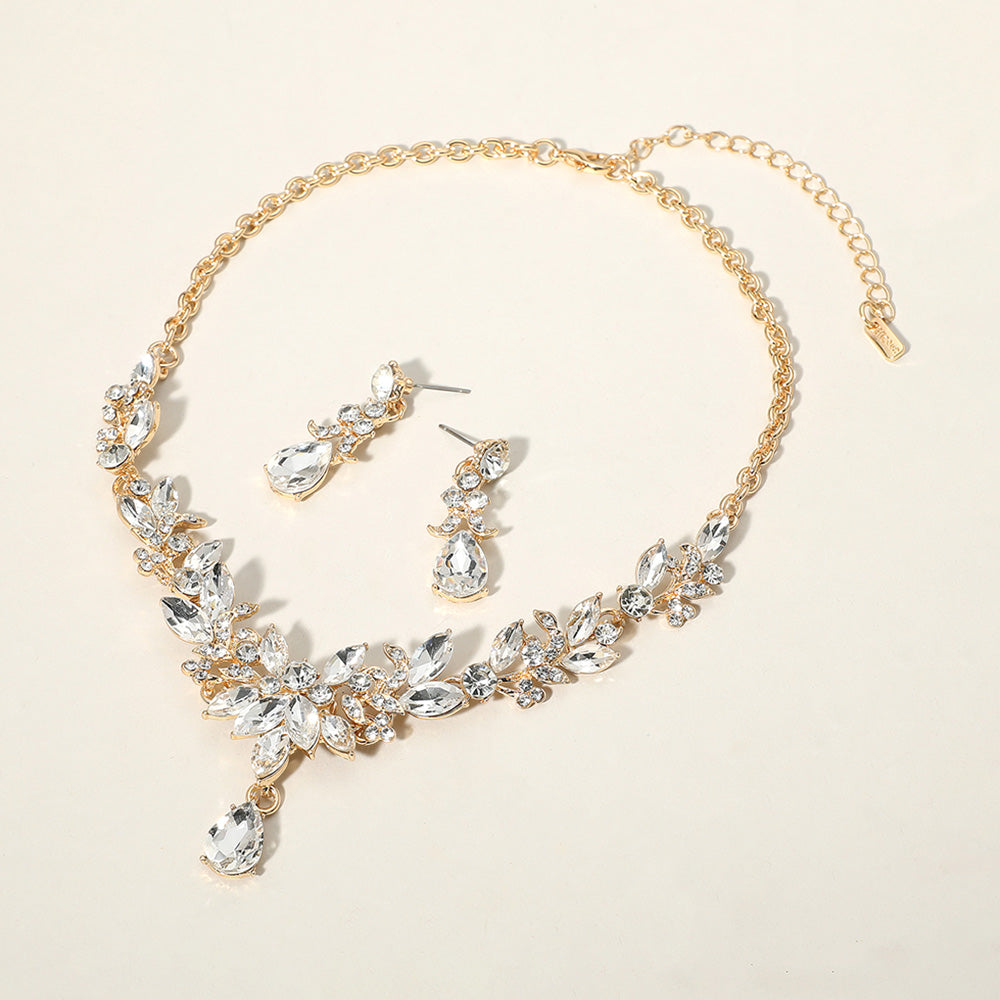 Clear crystal teardrop and marquise leaf necklace set on gold with matching earrings, elegant statement jewelry for bridal, prom, and evening wear on a beige background
