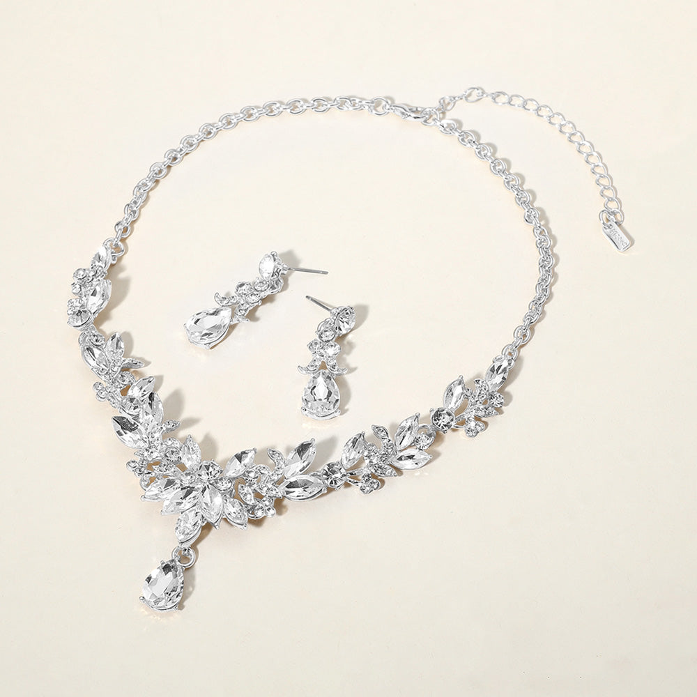 Clear crystal teardrop and marquise leaf necklace set on silver with matching earrings, elegant statement jewelry for bridal, prom, and evening wear on a beige background