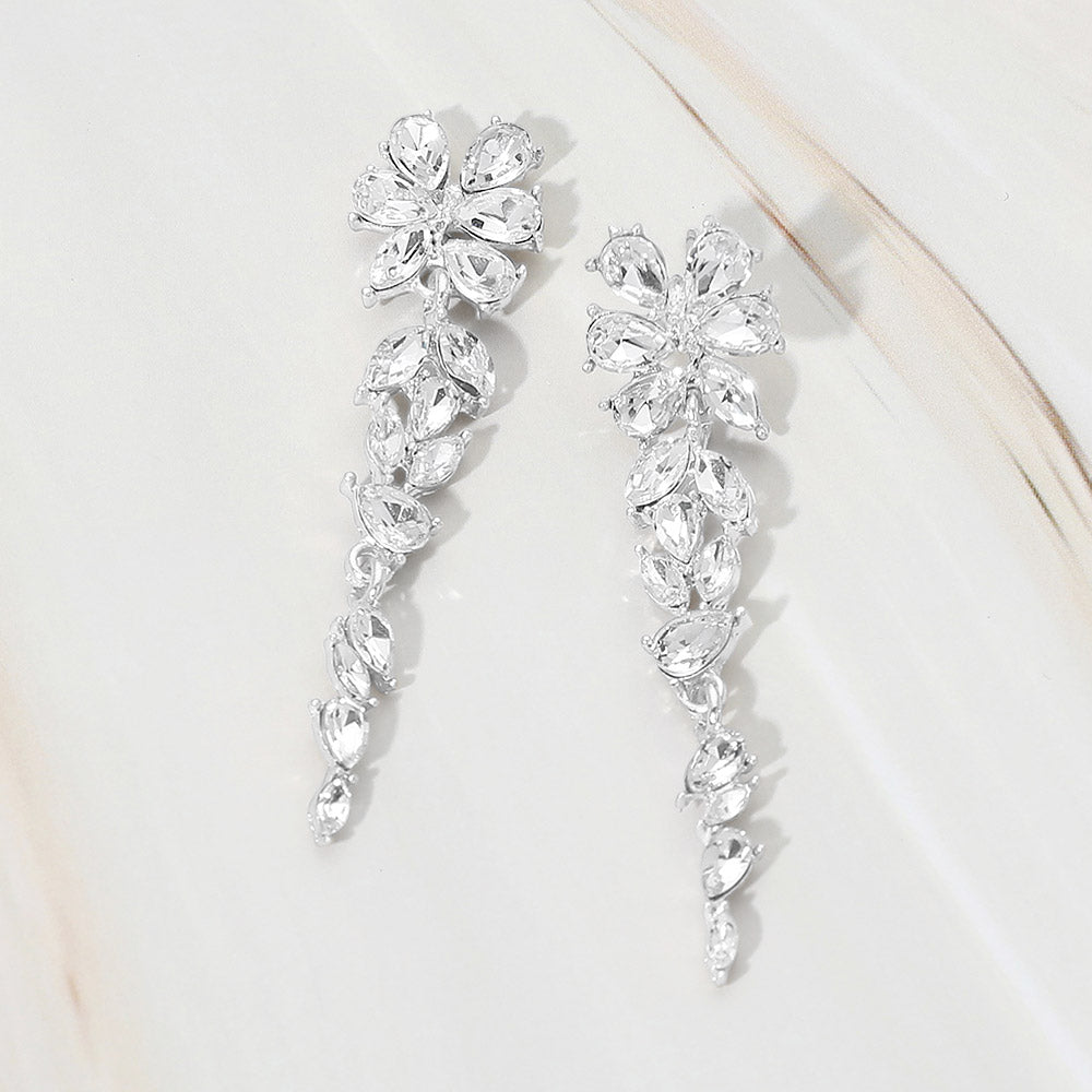 Silver-tone dangle earrings featuring clear marquise and round faceted crystals arranged in an elongated floral vine design, displayed on a white background.