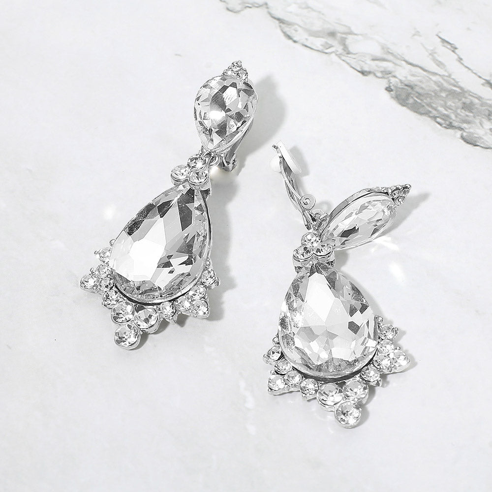 Clear faceted teardrop clip-on statement earrings on silver on a white marble background