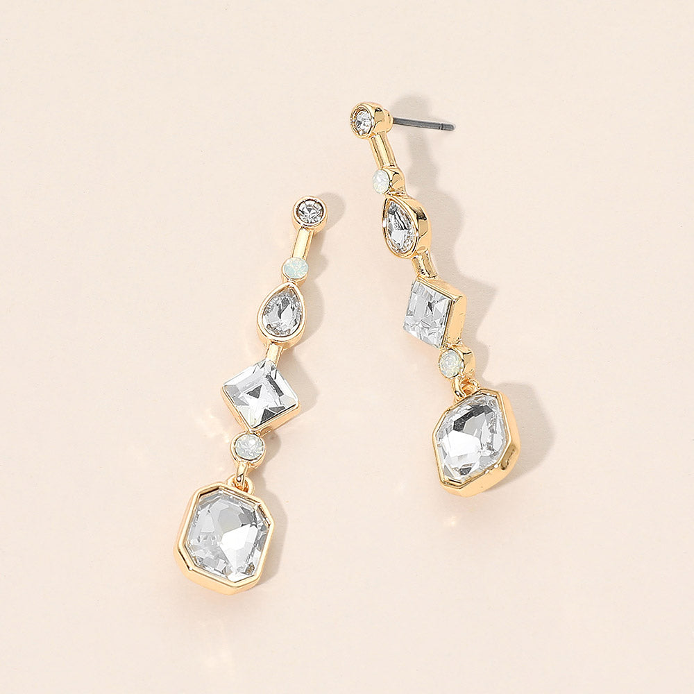 A pair of gold drop geometric earrings with clear faceted gemstones in a graduated dangle design, displayed on a light beige background.