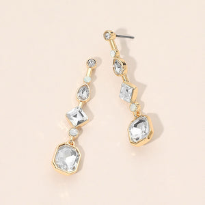 A pair of gold drop geometric earrings with clear faceted gemstones in a graduated dangle design, displayed on a light beige background.