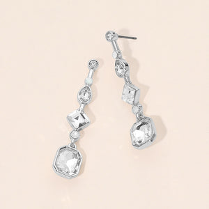 Clear geometric crystal link drop earrings on silver with faceted stones on a beige background.