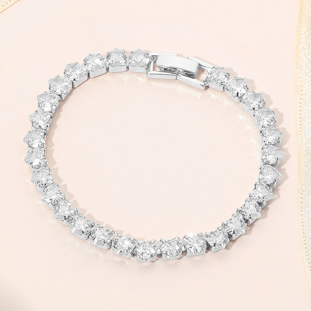 Clear crystal heart tennis bracelet in a silver finish featuring a continuous row of heart-shaped clear crystals with a fold-over clasp, displayed on a light jewelry background.