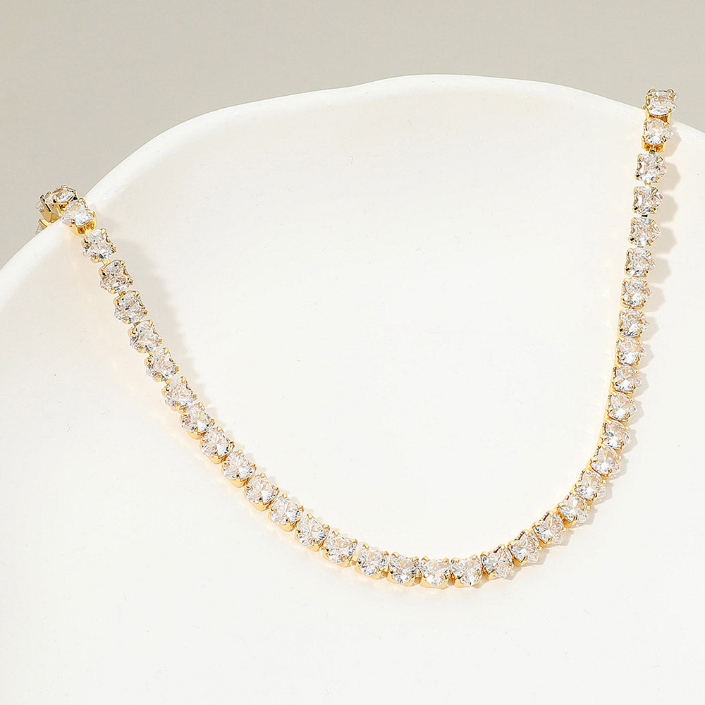 Clear crystal heart tennis necklace in a gold finish featuring a continuous row of heart-shaped clear crystals, displayed on a white jewelry display.