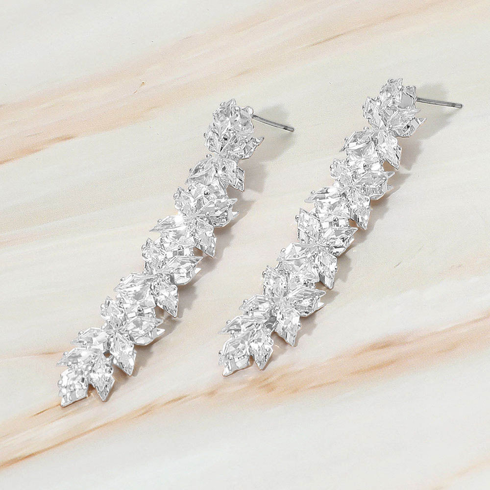 Pair of silver earrings with clear gemstones on a light wooden surface