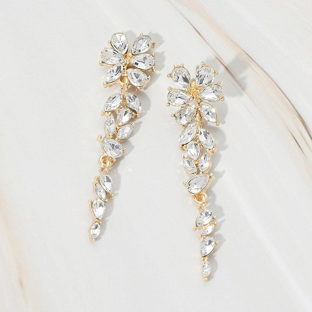 Gold-tone dangle earrings featuring clear marquise and round faceted crystals arranged in an elongated floral vine design, displayed on a white background.