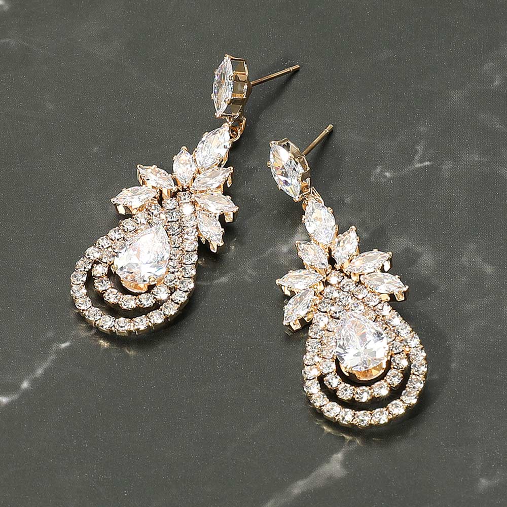Pair of ornate earrings with clear gemstones on gold pictured on a dark marble background
