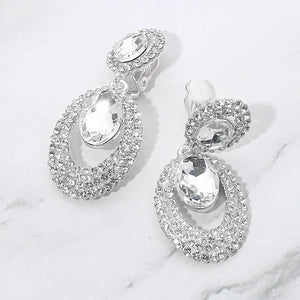 Clear oval double-halo crystal clip-on earrings on silver on a white marble background — 2.1" silver statement drops for evening or pageant glam.