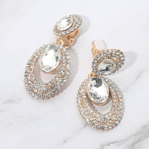 Clear oval double-halo crystal clip-on earrings on gold on a white marble background — 2.1" statement drops for evening or pageant glam.