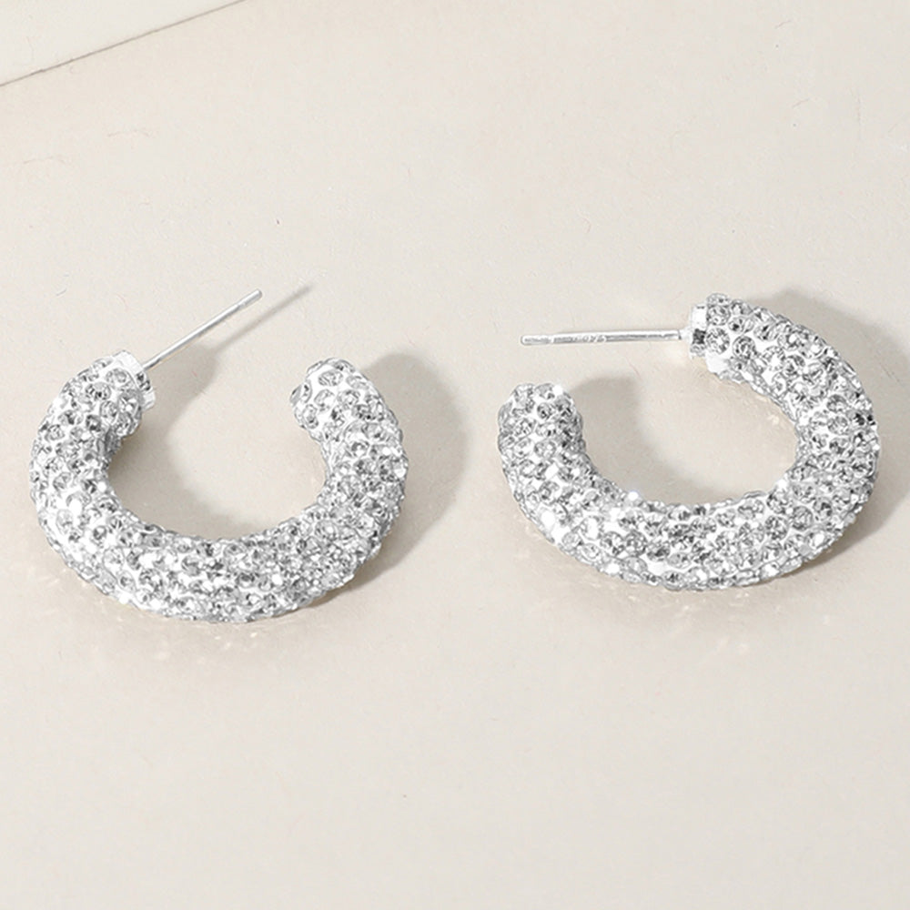 Clear crystal pavé half hoop earrings in a silver finish featuring rows of clear rhinestones covering the front of each hoop, displayed on a light beige background.